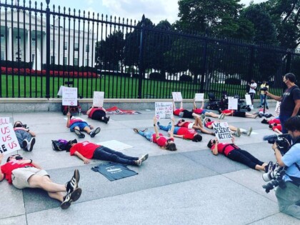Multiple people laying on the sidewalk holding signs in front of the White House